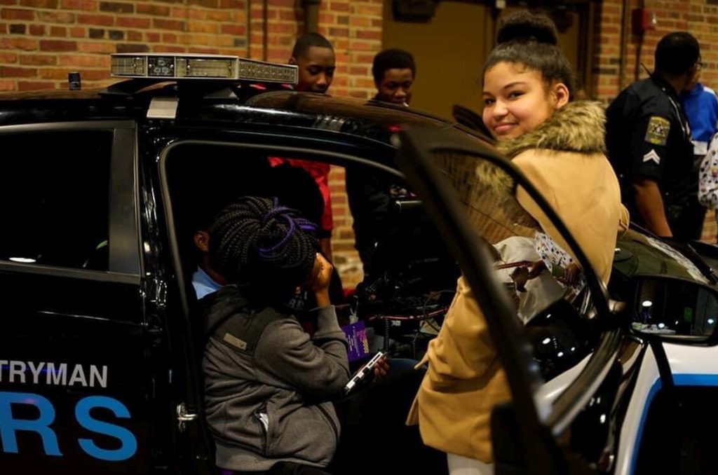 A woman in a brown coat smiling near a car door.