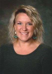 Smiling woman with blonde hair and green earrings.