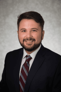 Professional headshot of a smiling man in a suit and tie.