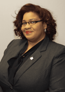Professional woman in a dark blazer with glasses and a confident smile.