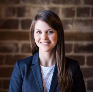 Professional woman smiling against a brick wall backdrop.