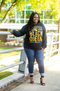A confident woman wearing a "Created Black Queen" sweatshirt outdoors.