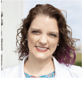Smiling woman with curly hair and purple highlights.