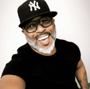 Smiling man in a black shirt and New York Yankees cap.