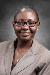 Professional woman in glasses smiling warmly in a studio portrait.