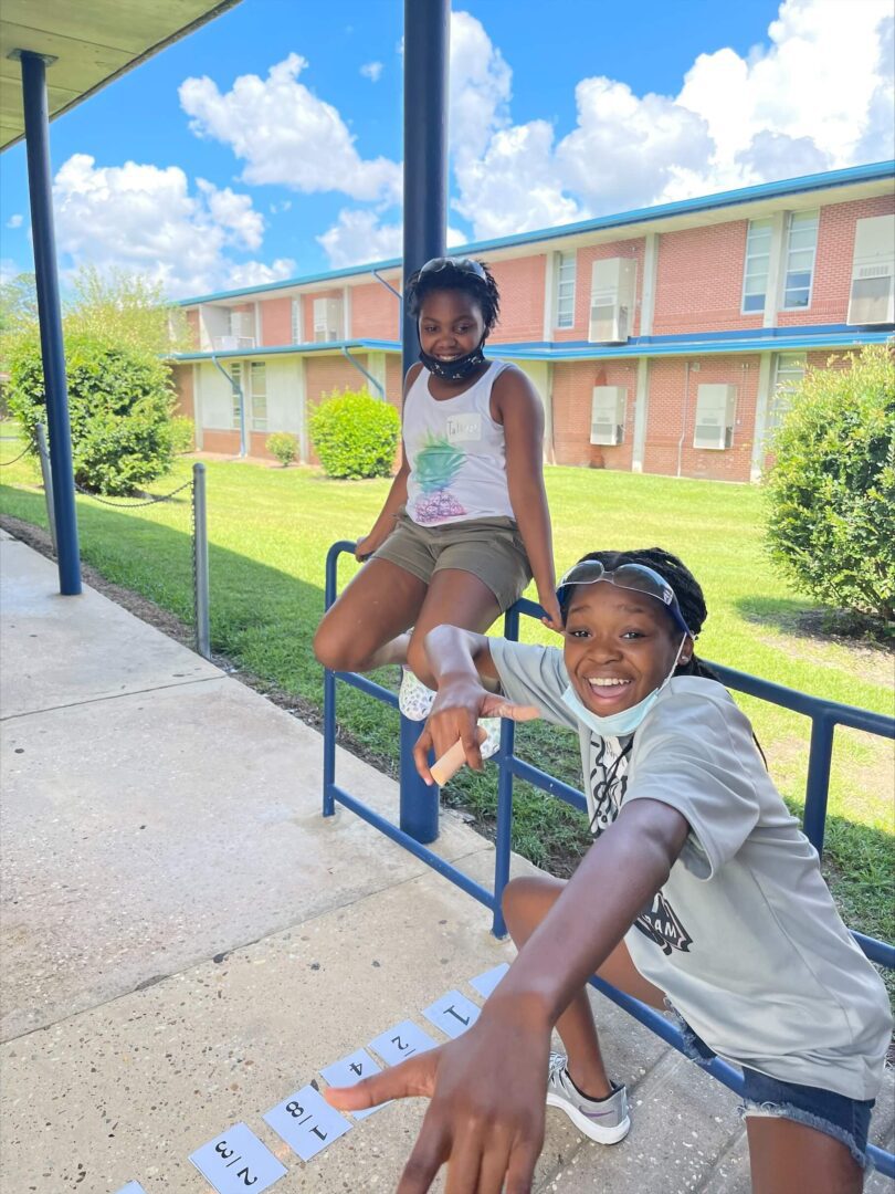 Two boys smiling and posing by a railing outside a school building.