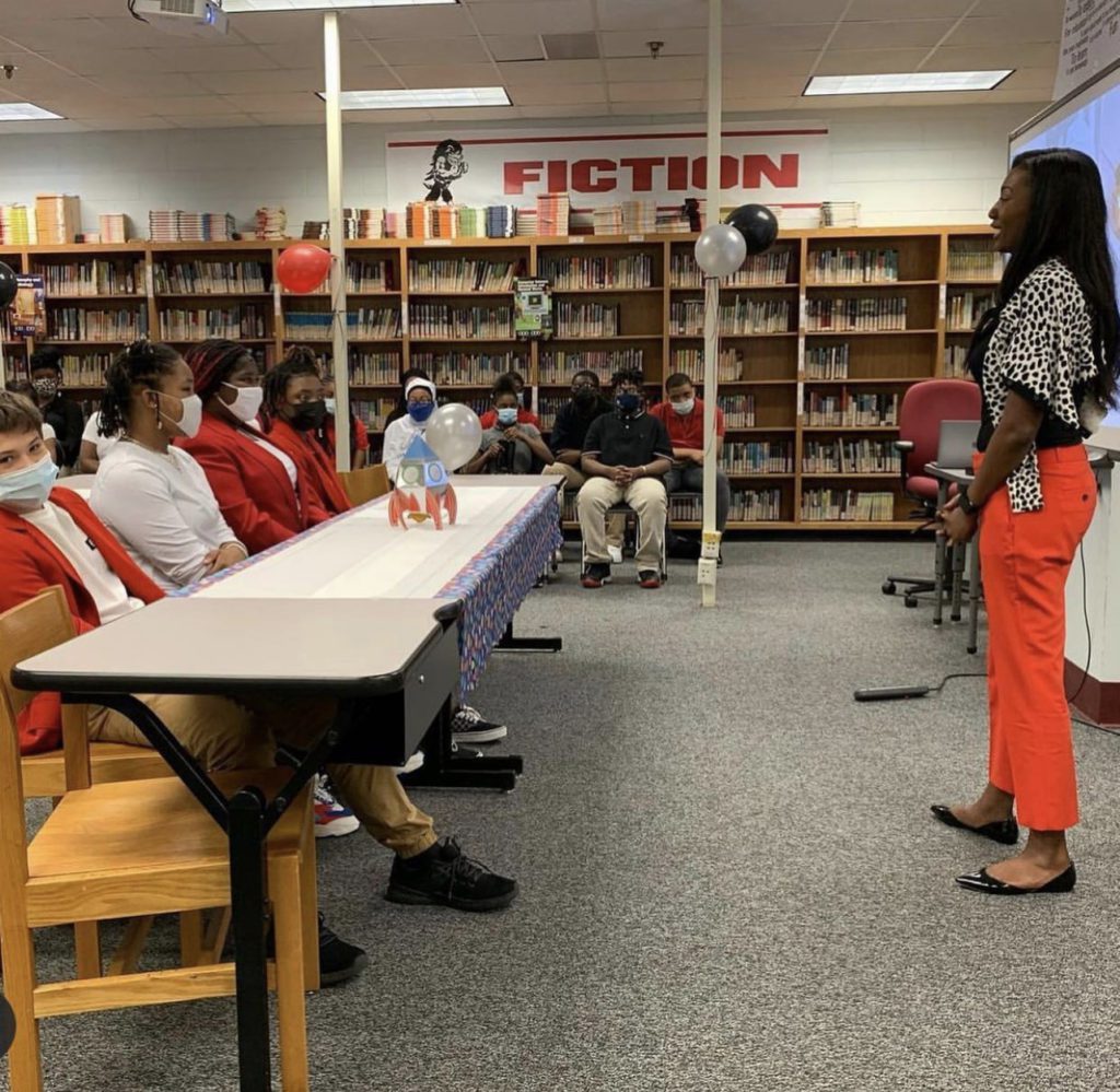 A woman speaks to students seated in a library classroom.