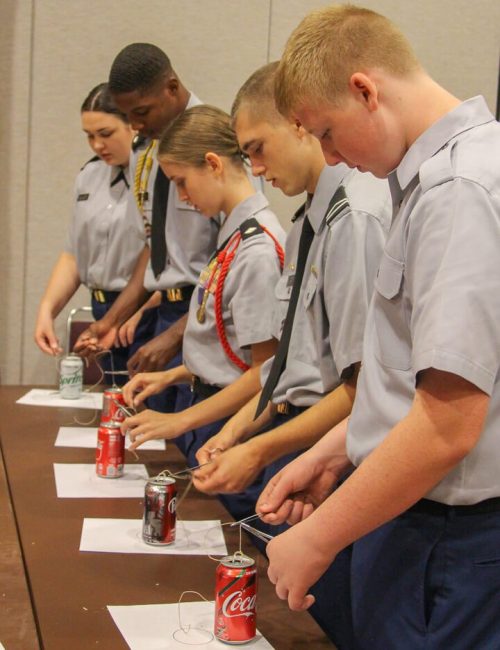 Young scouts in uniform preparing drinks at a table.